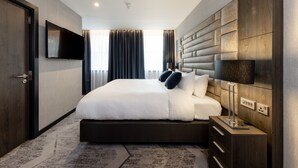 Een moderne hotelkamer met een groot bed, een flatscreen televisie aan de muur, een nachtkastje met een lamp, en een ingebouwd hoofdbord.