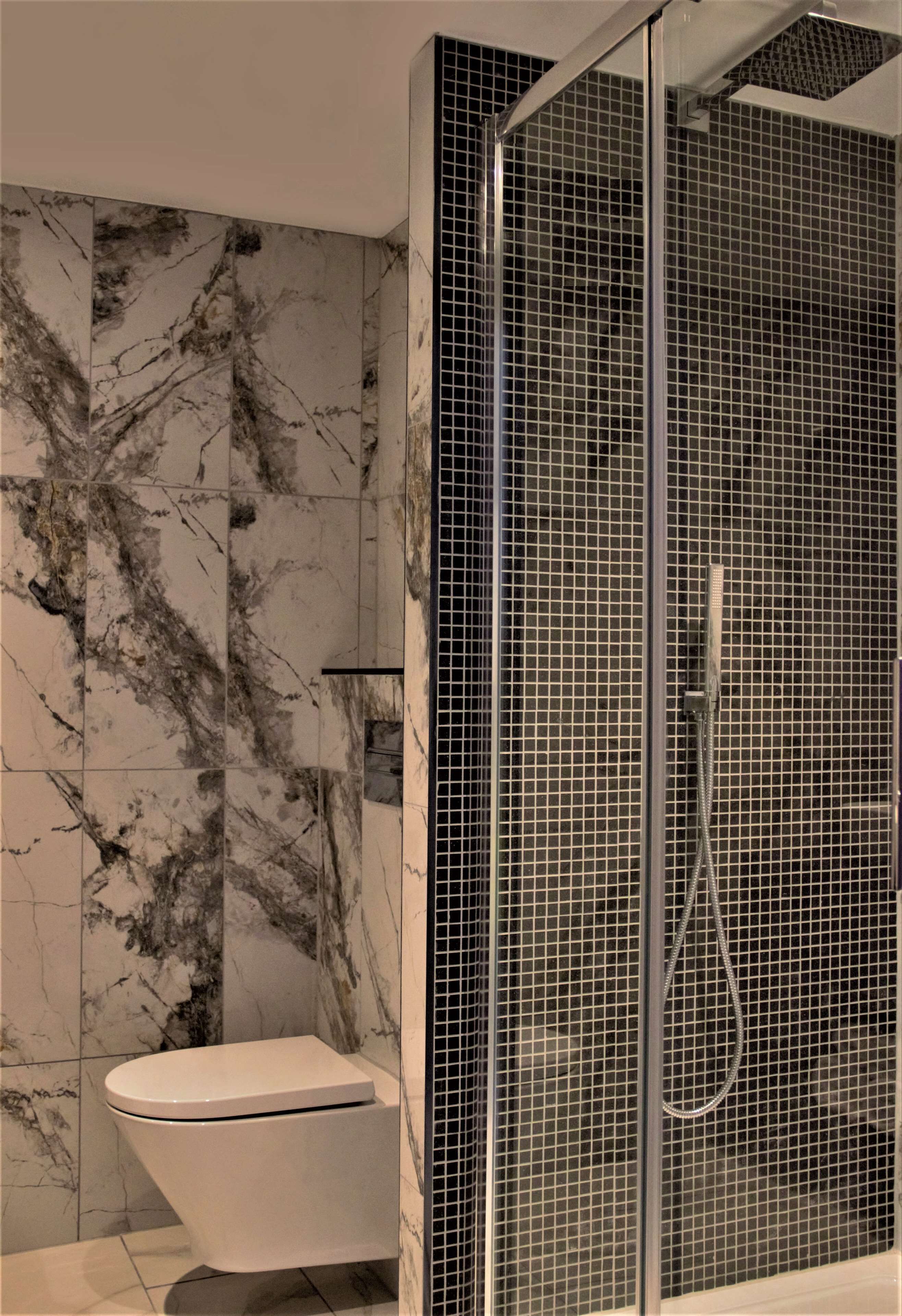 Ein Badezimmer mit Marmorwand, Duschkabine aus Glas und Toilette.