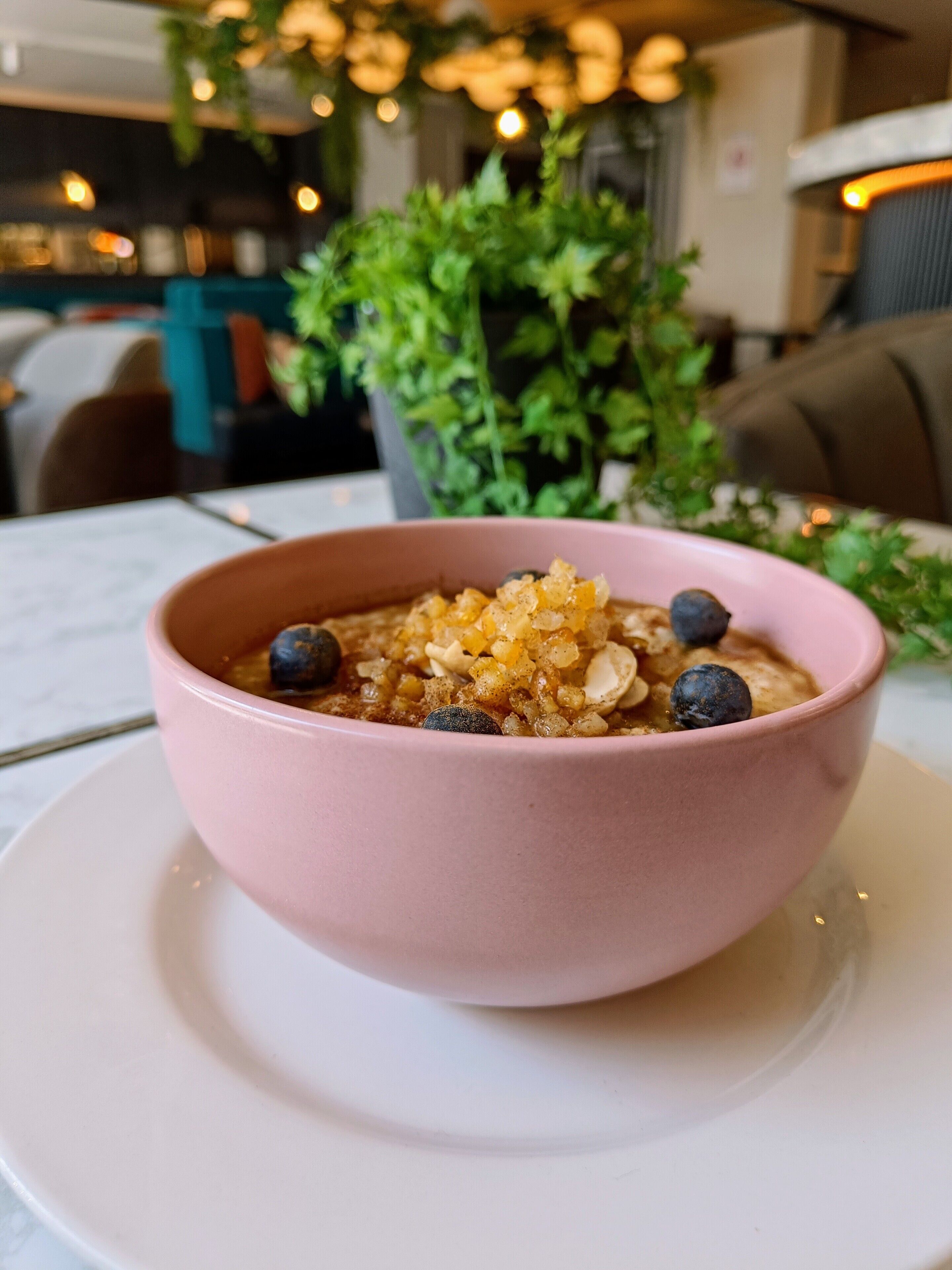 Eine rosa Schüssel Haferflocken mit Blaubeeren und Mandeln auf einem weißen Teller.