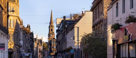 A historic street with a prominent church tower, vintage buildings, and parked cars.