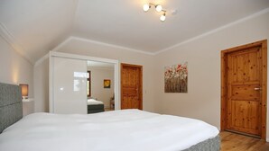 Un dormitorio con una cama grande, puertas de madera, un cuadro y una lámpara en el techo.