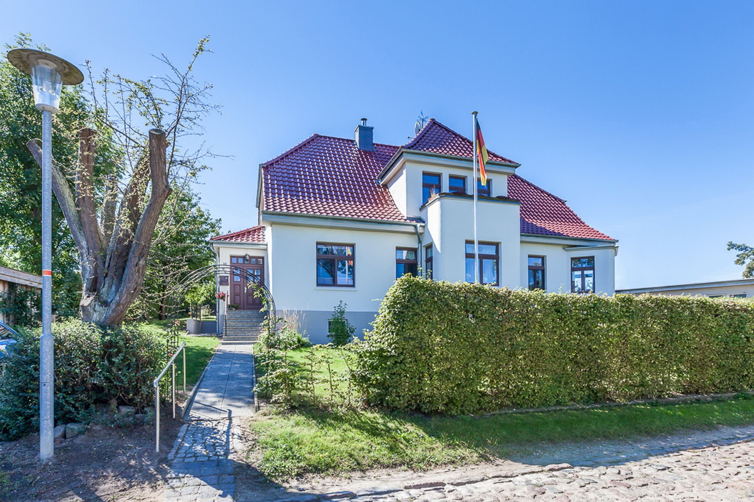 Ein zweistöckiges Haus mit rotem Ziegeldach, einer Fahnenstange und einem gepflegten Garten.