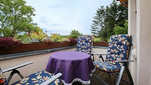 Un área de estar al aire libre con una mesa cubierta con un mantel morado y dos sillas con estampado de hojas.