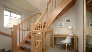 Un escalier en bois avec des marches recouvertes d’une moquette grise, un bureau en bois avec une chaise blanche et des tableaux encadrés accrochés au mur.