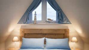 Une chambre à coucher avec une tête de lit en bois, un lit avec une literie bleue, deux lampes de chevet, une fenêtre avec des rideaux bleus et un petit objet décoratif posé sur le rebord de la fenêtre.