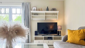 Un salon avec un téléviseur, des étagères blanches, un canapé et une table basse en verre.