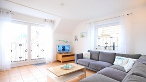 Ein modernes Wohnzimmer mit einem grauen Sofa, einem Holztisch und einem Fernseher auf einem Holzschrank.
