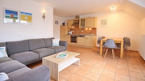 Ein modernes Wohnzimmer mit grauem Sofa, einem Holztisch und einem Essbereich mit Holztisch und Stühlen.