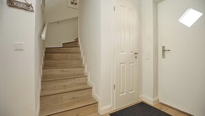 A staircase leading to a white door with a small window, a wooden floor, and a wall-mounted sign. - Reet/am09b Reethaus Am Mariannenweg 09b (Boltenhagen)