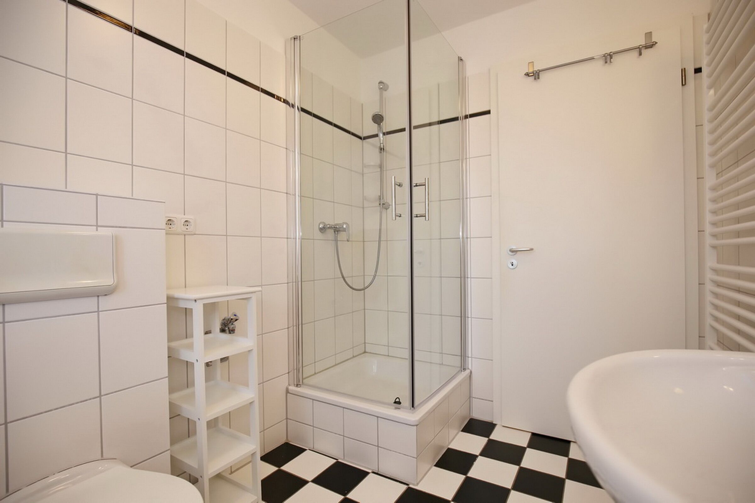 Une salle de bain avec une douche à parois de verre, un lavabo blanc et un carrelage à motifs géométriques.