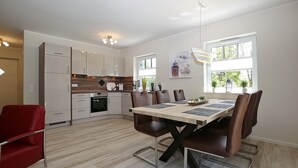 Una cocina moderna con armarios blancos, una mesa de comedor con sillas y una silla roja.