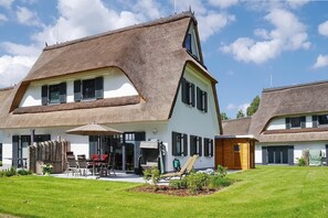 Une maison avec un toit à forte pente, une véranda à l’avant avec une table et des chaises, et un petit jardin.