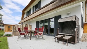 Un patio exterior con una mesa de comedor y sillas, una parrilla y una zona de estar cubierta.