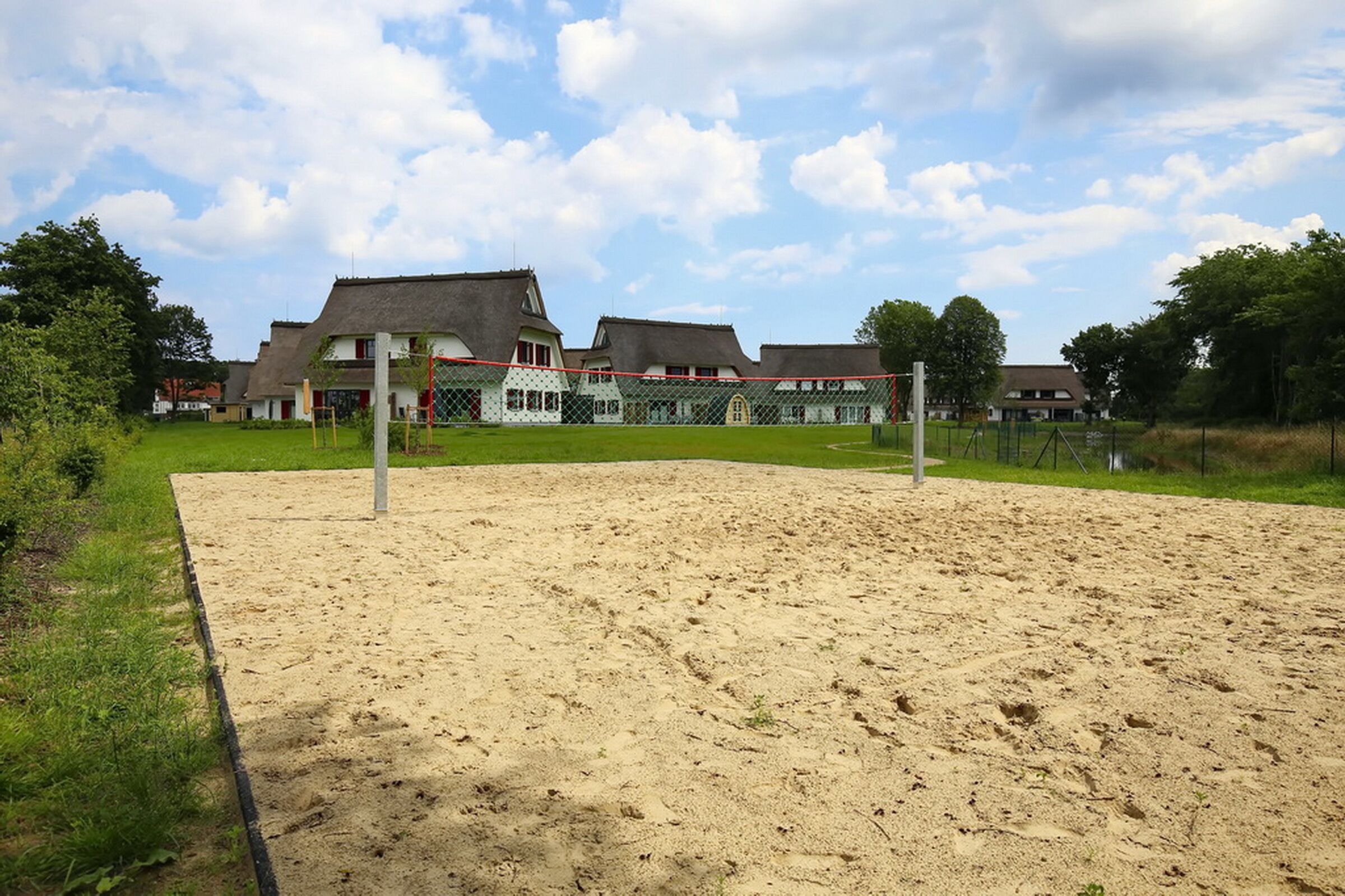 En sandvolleyballbane med net, omgivet af et hegn, og huse i baggrunden.