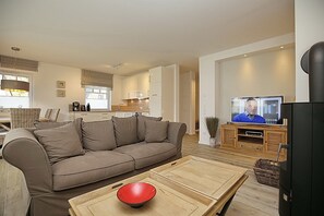Ein modernes Wohnzimmer mit einem beigen Sofa, einem Holztisch und einem Fernseher.