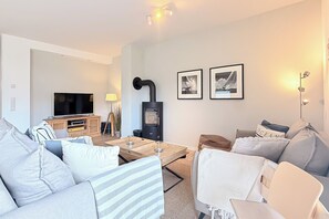 A modern living room with a flat-screen TV, a wood-burning stove, and two framed pictures on the wall.