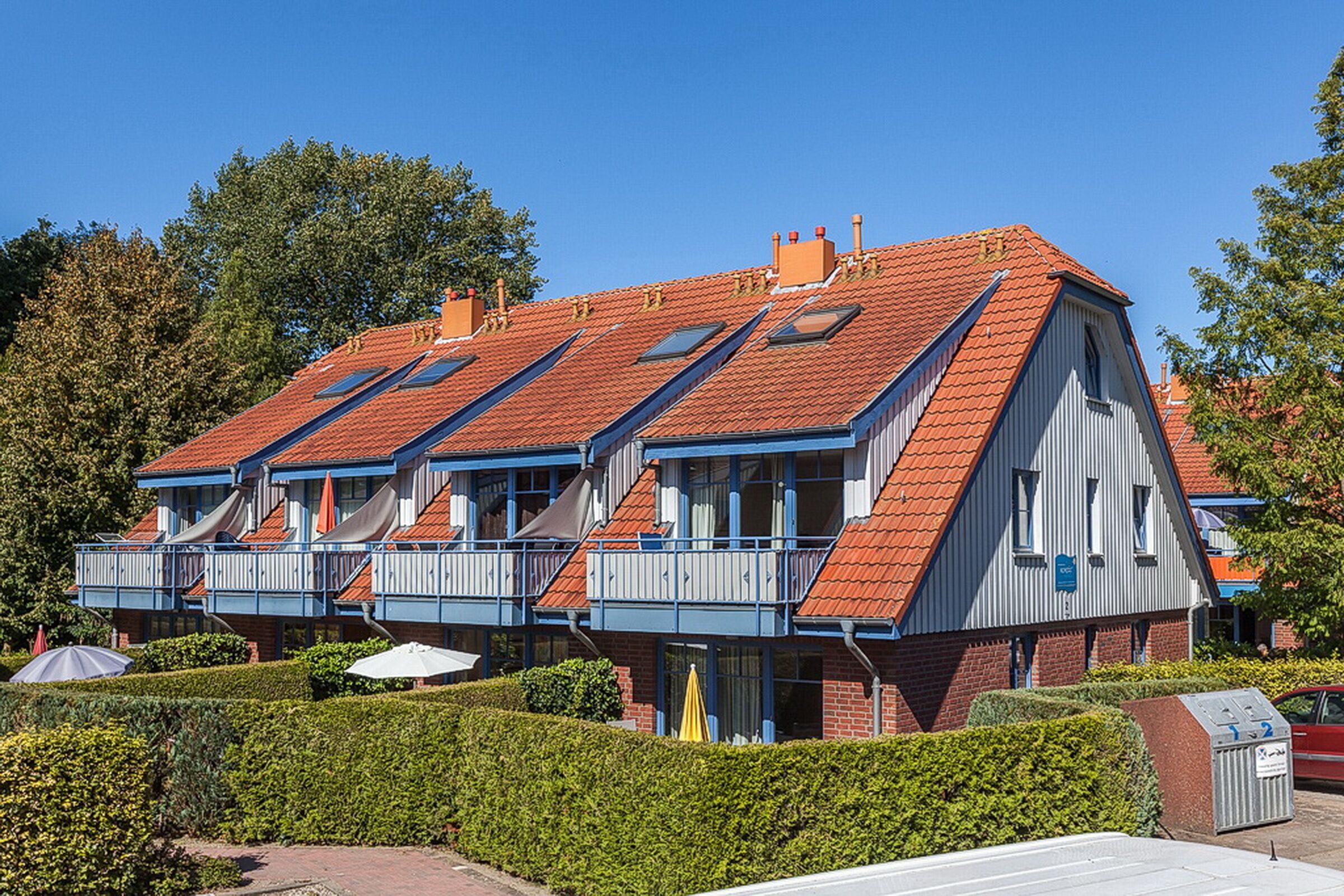 Een meerlaags gebouw met een dak van rode tegels, balkons en een baksteenvoorgevel.
