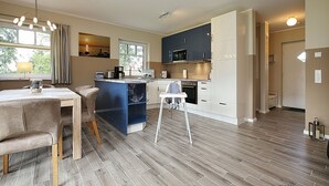 Una cocina moderna con comedor, una isla azul y una trona blanca.