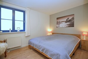 Una camera da letto con un letto, una finestra, un termosifone, una lampada e un quadro appeso al muro.