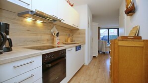 Moderni keittiö, jossa on valkoiset kaapit, sisäänrakennettu uuni ja puinen työtaso.