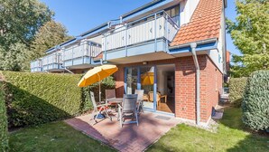 Ein zweistöckiges Haus mit einem Balkon, einer Terrasse und Gartenmöbeln sowie einem gepflegten Garten.
