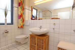 A bathroom with a white sink, toilet, and wooden cabinet. - Papillon Wohnung 02-1 (Ostseebad Boltenhagen)
