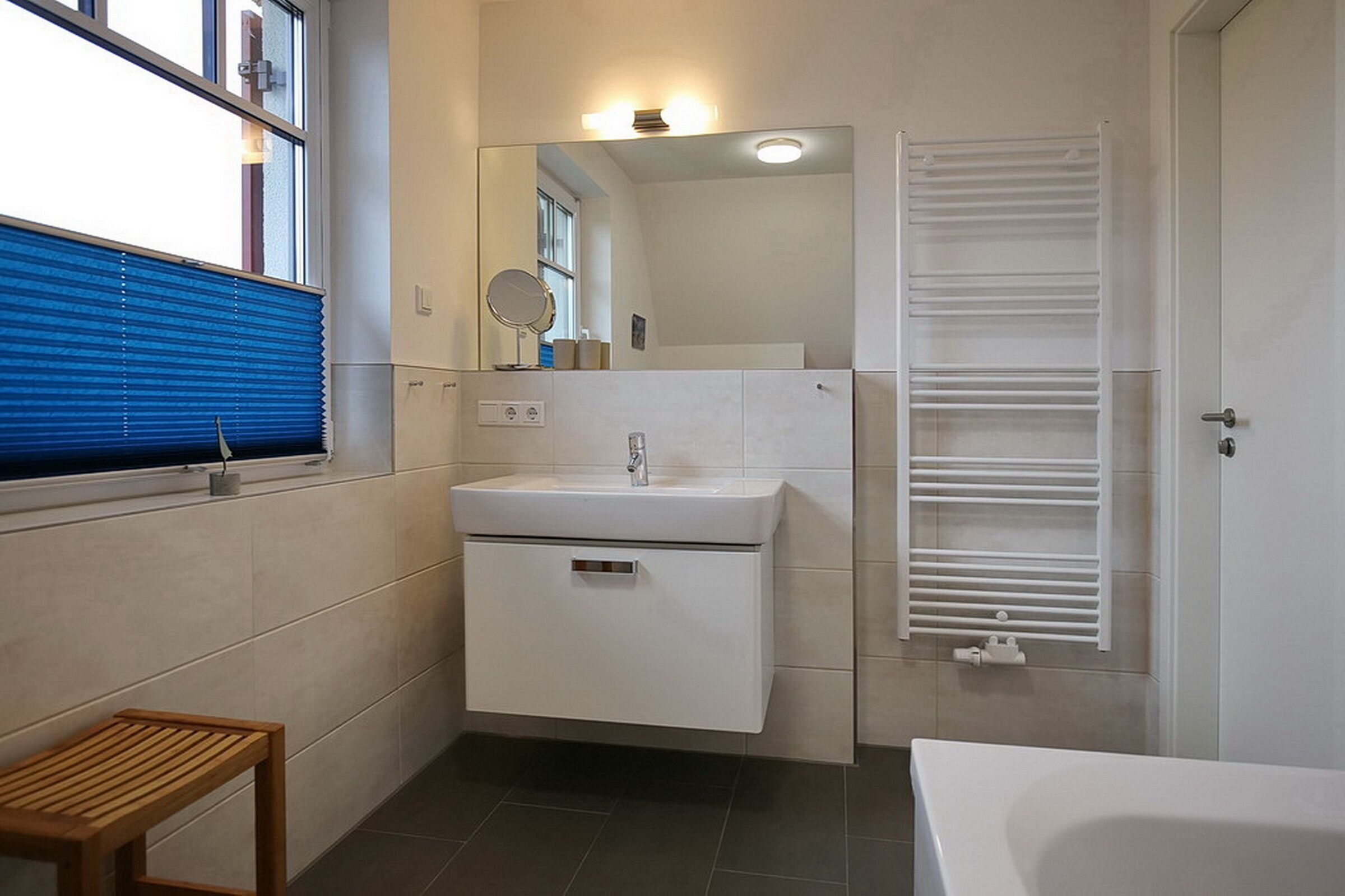 Ein modernes Badezimmer mit integriertem Waschbecken, einem Spiegel, einem Handtuchhalter und einem hölzernen Hocker.