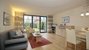 Ein modernes Wohnzimmer mit grauem Sofa, einem Couchtisch und einem Essbereich mit weißem Tisch und Stühlen.