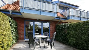 Eine Terrasse mit Tisch und Stühlen, eine Ziegelwand und ein blauer Balkon.