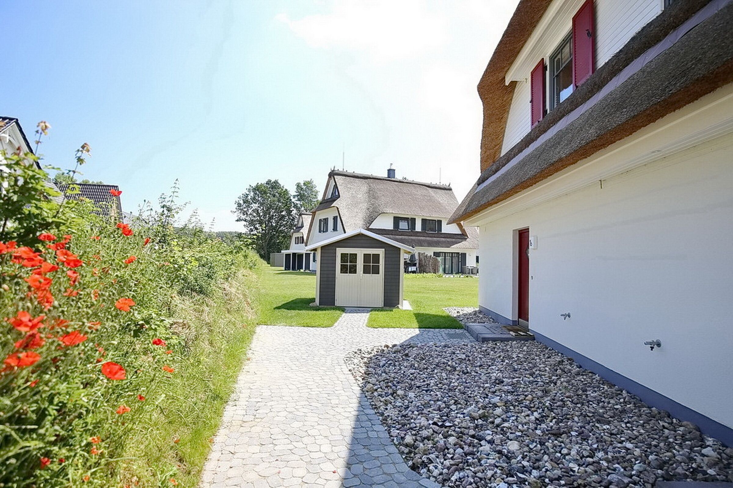 A house with a paved driveway leading to a garage, surrounded by a gravel area and a flower bed.