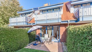 A two-story house with a balcony, a patio with a table and chairs, and a well-maintained garden. - Papillon Wohnung 02-3 (Ostseebad Boltenhagen)