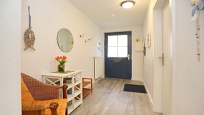 A hallway with a wicker chair, a small table with a vase of flowers, a mirror, and a blue door. - Papillon Wohnung 02-3 (Ostseebad Boltenhagen)