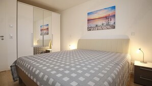 Un dormitorio con cama, mesita de noche, lámpara, un cuadro, armario y espejo.