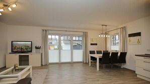 Una sala de estar moderna con televisor de pantalla plana, comedor con mesa y sillas, y cocina con mostrador y alacenas.