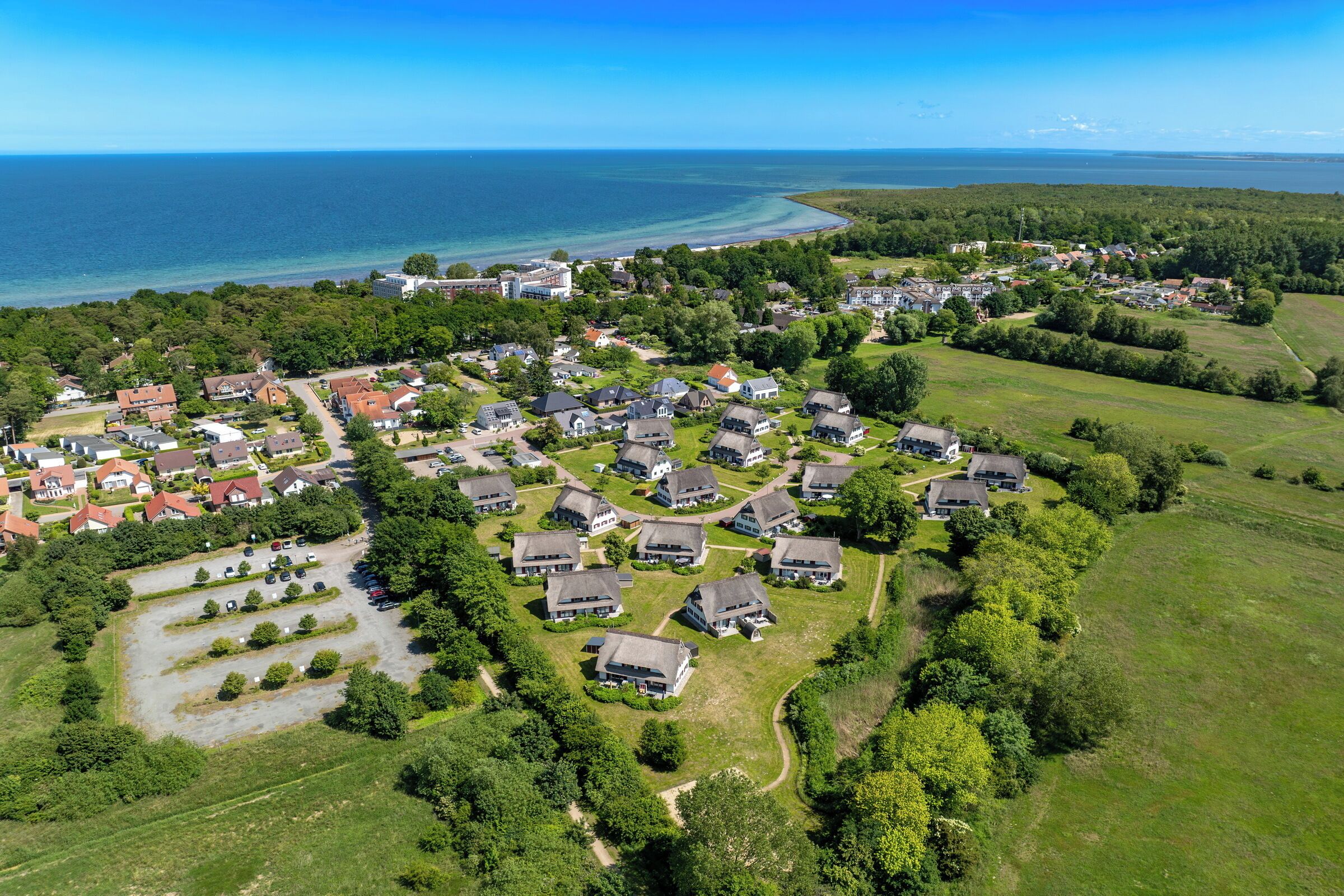 An aerial view of a residential area with houses, green spaces, and a coastline.