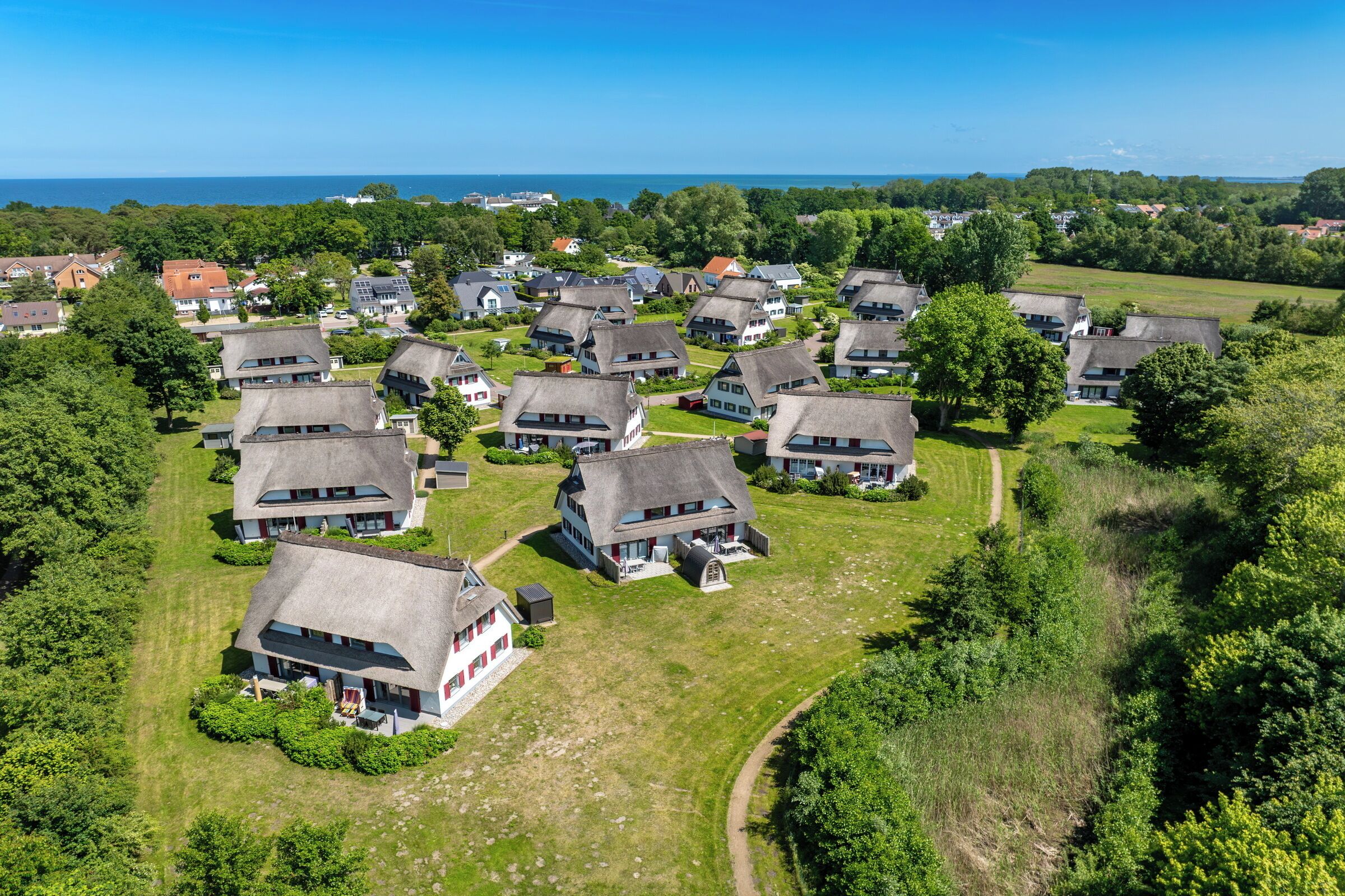 Overzicht vanuit de lucht van een woonwijk met meerdere huizen, elk met een vergelijkbare architectuur, schuine daken en omringd door groen.