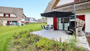 Una casa moderna con techo de paja, un patio con mobiliario exterior y un jardín cuidado.