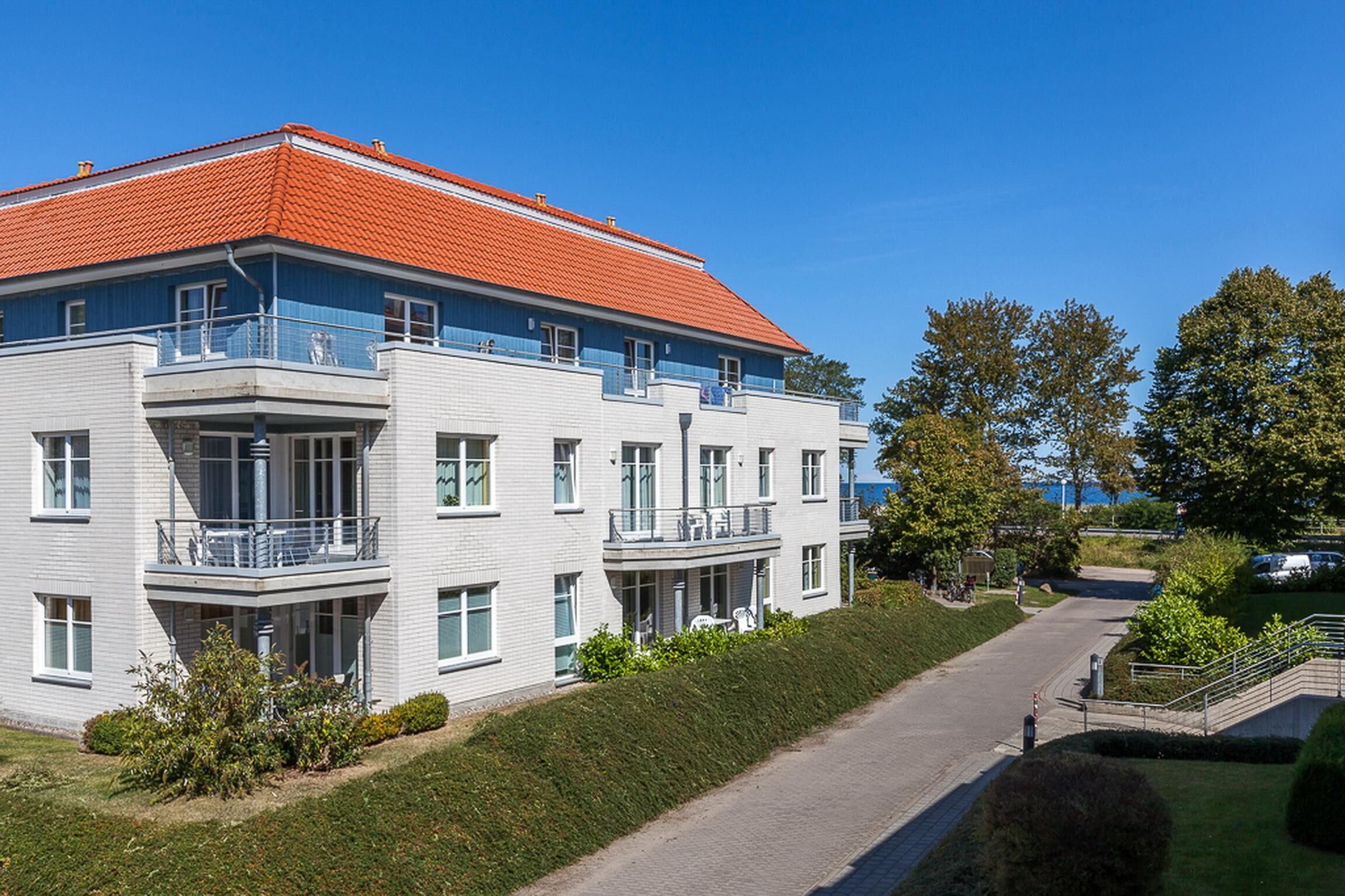 A multi-story building with a red roof, white walls, and balconies.