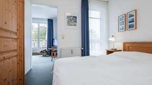 Una camera d'albergo con un letto grande, un armadio in legno, una scrivania con una sedia, una finestra con tende e quadri appesi al muro.
