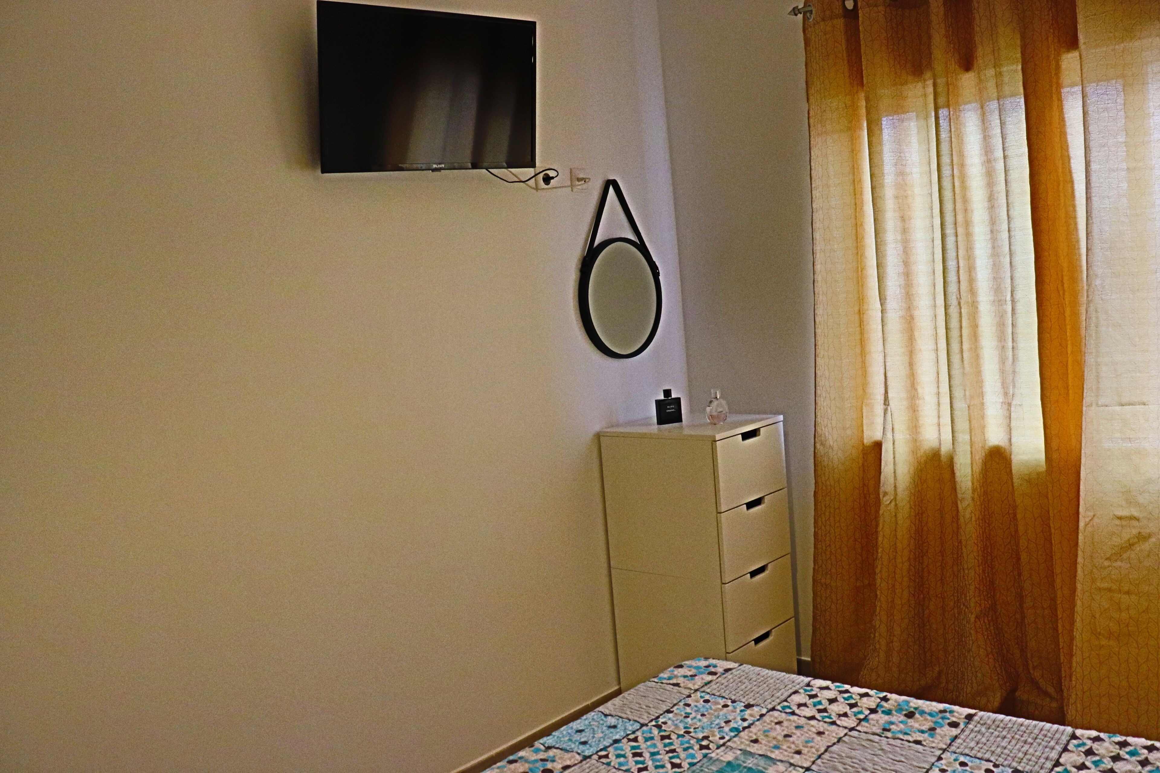 A bedroom with a bed, a dresser, a mirror, and a television mounted on the wall.