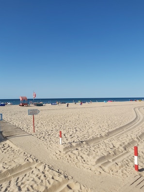 Ein sandiger Strand mit blauem Himmel, einem Rettungsturm und einem Schild mit Strandregeln.