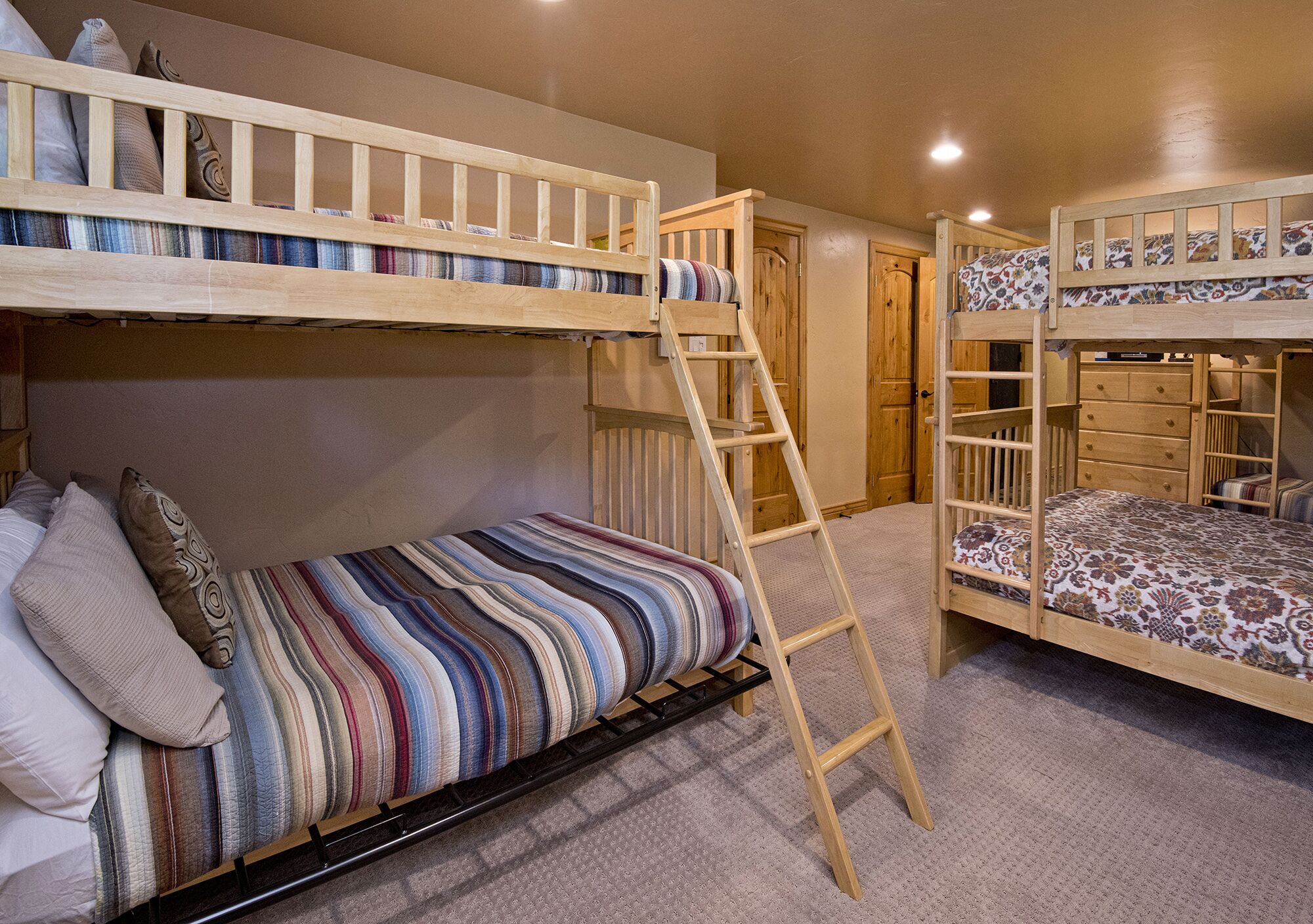 A bunk bed room with a ladder, a lower bed with pillows, and a door in the background.