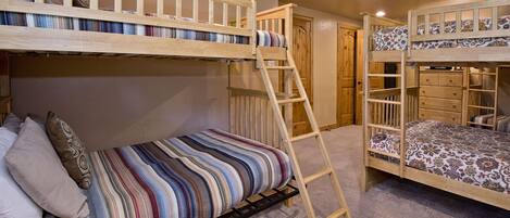 A bunk bed room with a ladder, a lower bed with pillows, and a door in the background.