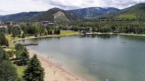 A lakeside resort with a sandy beach, a dock, and a view of mountains in the background. - Spacious Avon Retreat | Pool, Tennis, 2 Masters & Free Shuttle (Avon)