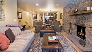 A living room with a fireplace, a sofa, armchairs, a coffee table, and a kitchen in the background. - Spacious Avon Retreat | Pool, Tennis, 2 Masters & Free Shuttle (Avon)