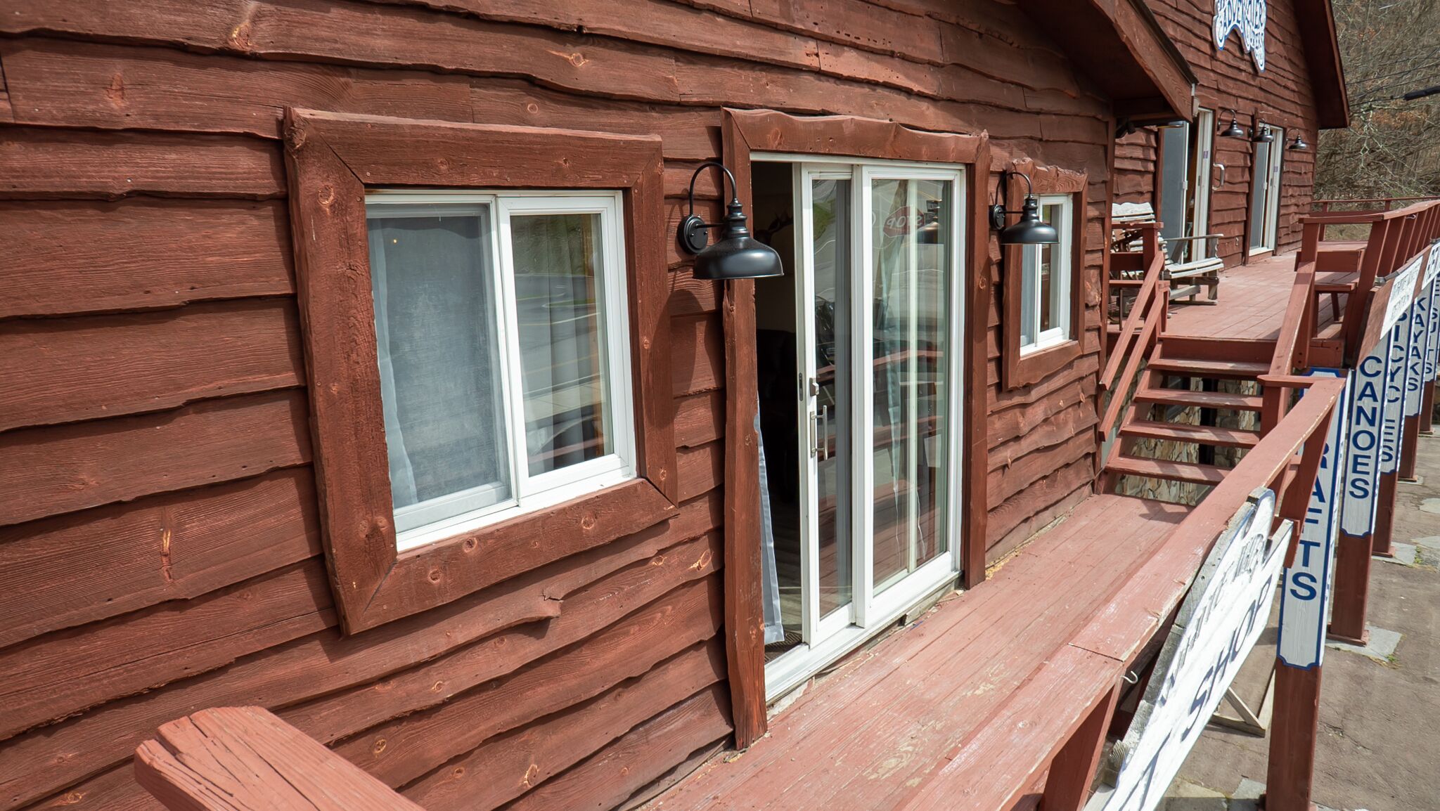 A rustic wooden cabin with large windows, a porch with a bench, and a sign indicating a canoe rental service.