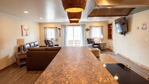 A spacious living area with a long central island, a sofa set, a television, and a kitchen area with a stove.