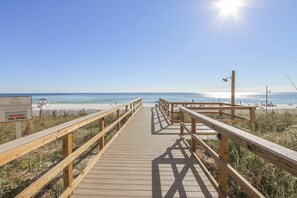 A wooden boardwalk leading to a beach with a clear sky and calm sea.