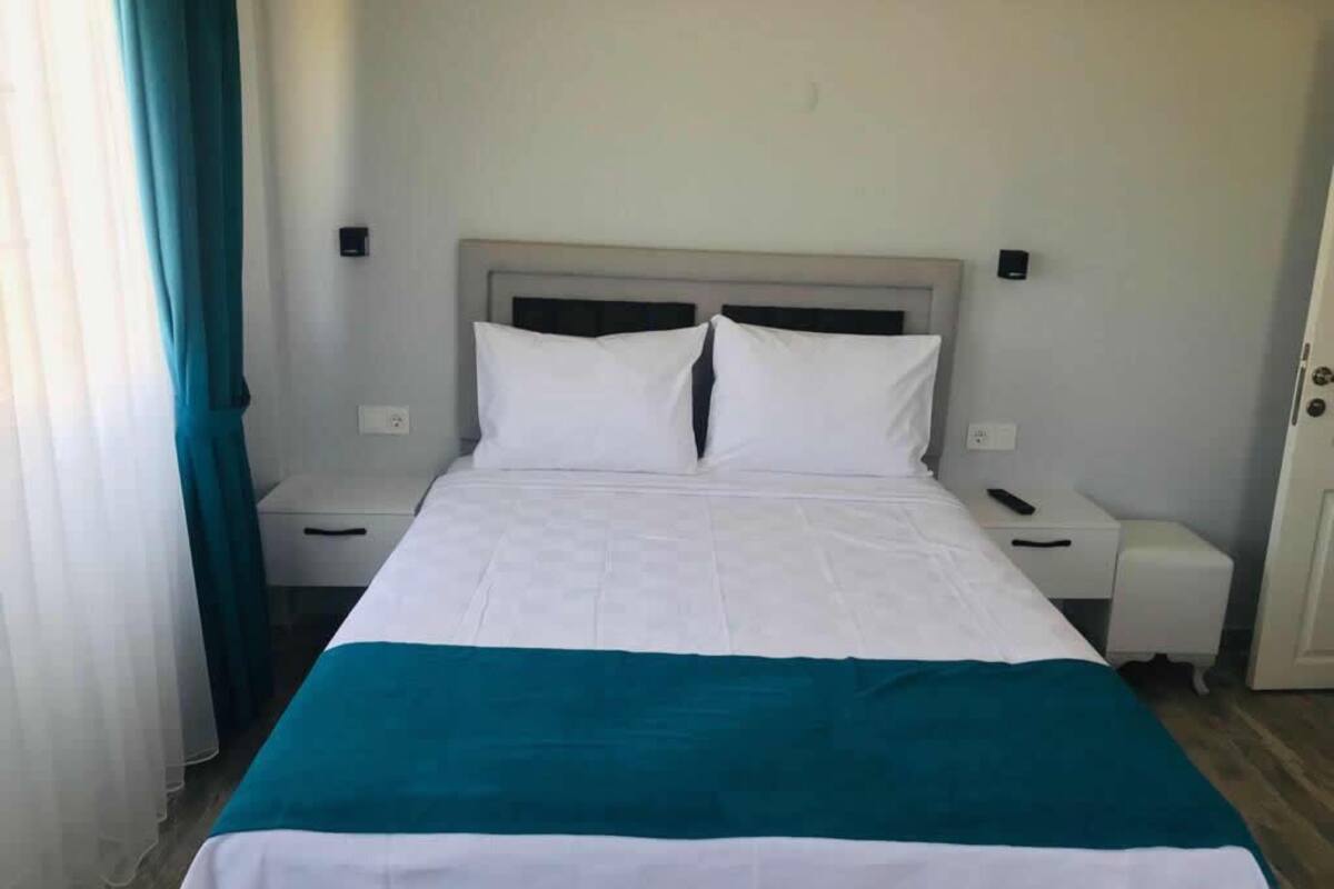 A hotel room with a bed, a nightstand, a drawer, and a door.