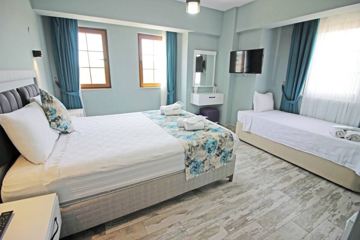 A hotel room with a large bed, a smaller bed, a TV, a mirror, and a window with curtains.